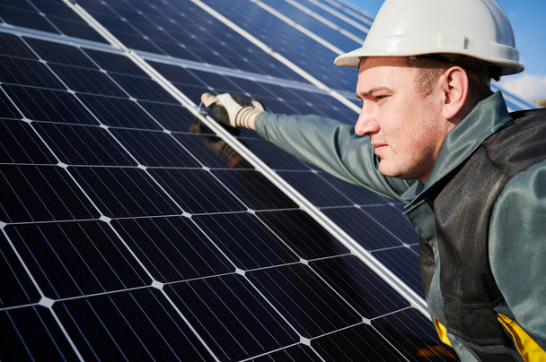 Großaufnahme eines männlichen Arbeiters, der Schutzanzug, Helm und Handschuhe trägt. Elektriker installieren an einem sonnigen Tag eine Photovoltaik-Solarbatterie. Konzept alternativer Energien und nachhaltiger Energiequellen. - Foto, Bild