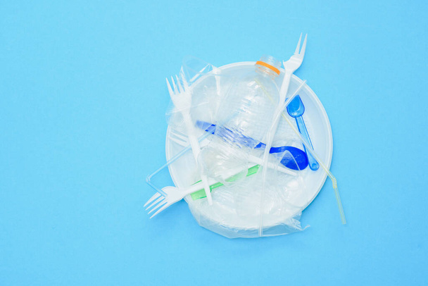 White single-use plastic and other plastic items on a blue background. The concept of choice without plastic or environmental problems. - Φωτογραφία, εικόνα