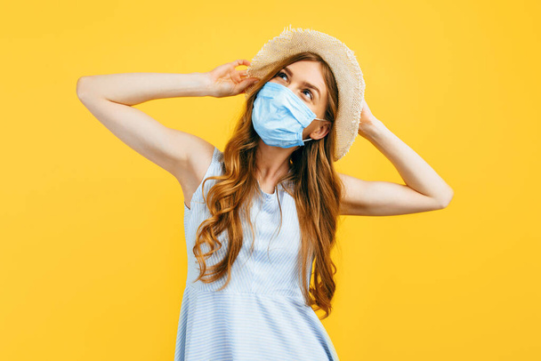 Portrait of a girl in a hat in summer, wears a medical protective mask against a viral infection, on a yellow isolated background. Quarantine, coronavirus, summer - Фото, зображення