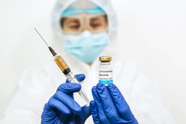 egy egészségügyi laboratóriumi dolgozó egy injekciós üveg vakcinát és egy fecskendőt tart magánál. Az orvos kezei közel vannak. Covid-2019-ben. 2020-as járvány. Vakcina a vírus ellen. Az orvos fehér köpenyben és kék kesztyűben.. - Fotó, kép