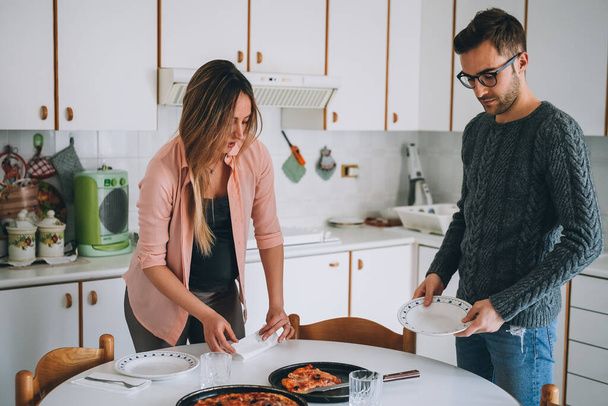 Pregnant couple indoors at home setting the table for lunch - parenthood, everyday life, togetherness concept - Photo, Image