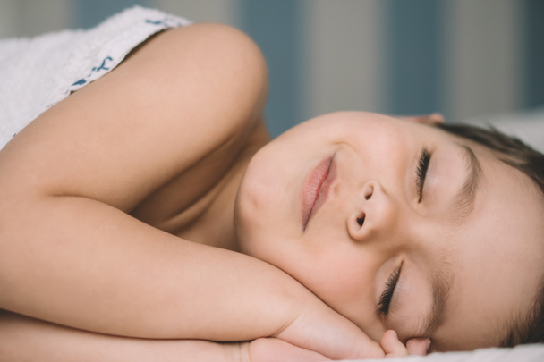 чарівний хлопчик посміхається під час ковзання в ліжку
 - Фото, зображення