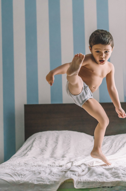 aranyos fiú szórakozás, miközben ugrás és rugdossa a lábát az ágyban - Fotó, kép