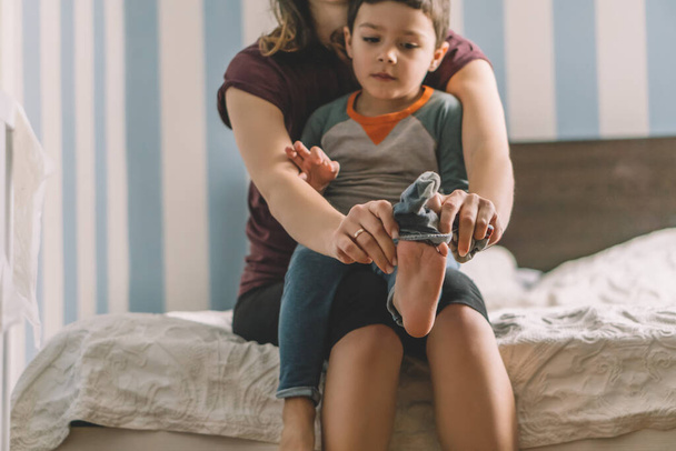 cropped view of woman dressing adorable son while sitting on bed - Foto, Imagen