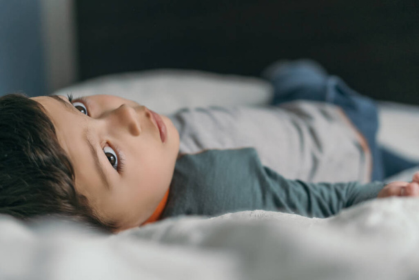 selective focus of thoughtful boy lying on bed at home and looking away - Foto, Bild