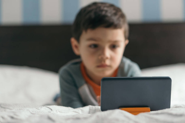 selective focus of cute, attentive boy looking at smartphone in bedroom - Photo, Image