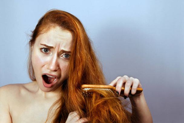 Woman brushing her problem tangled ginger hair with a wooden comb. - Foto, afbeelding