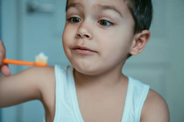 selektivní zaměření vzrušeného dítěte při pohledu na zubní kartáček se zubní pastou - Fotografie, Obrázek