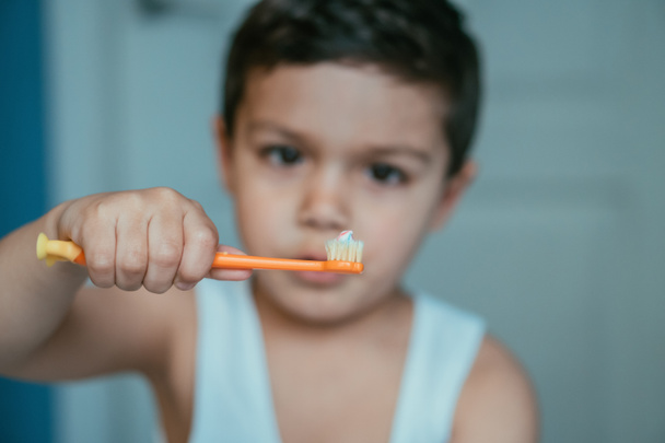 Diş fırçasına diş macunuyla bakan sevimli çocuğun seçici odağı. - Fotoğraf, Görsel