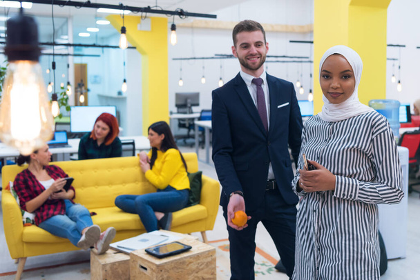 Portrait of young bearded Caucasian businessman dressed smart casual and african hijab woman posing inside modern coworking space. - Foto, Imagem