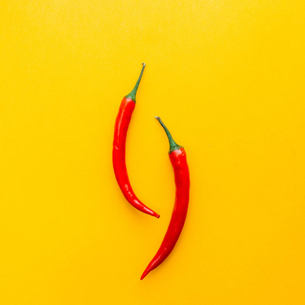 Two red chili peppers on yellow surface flatlay - Zdjęcie, obraz