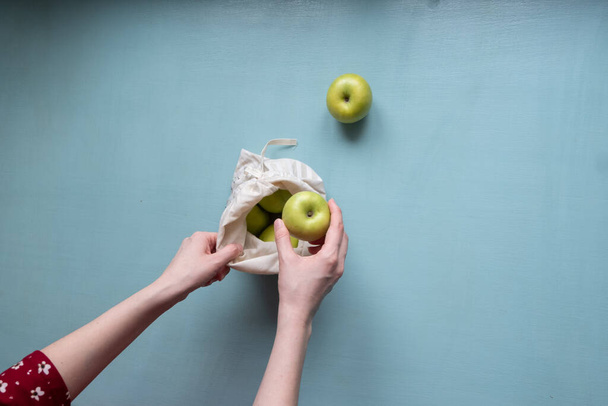 Process how hands of a young woman puts apples in a reusable bag. View from above. Empty space for text on the right. - Фото, зображення
