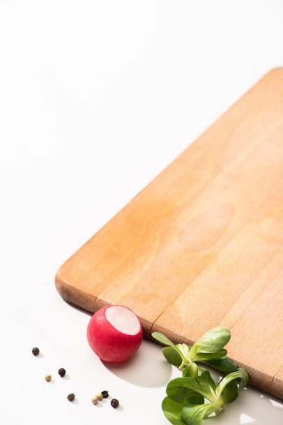 delicious radish and greens with black pepper near wooden board on white background - Photo, Image