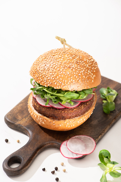deliciosa hamburguesa vegana con rábano y rúcula sobre tabla de madera con pimienta negra sobre fondo blanco
 - Foto, Imagen