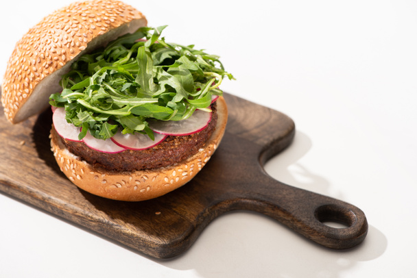 delicious vegan burger with radish and arugula on wooden board on white background - Photo, Image