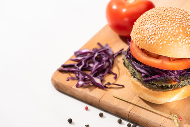 delicious vegan burger with red cabbage and tomato on wooden board with black pepper on white background - Photo, Image