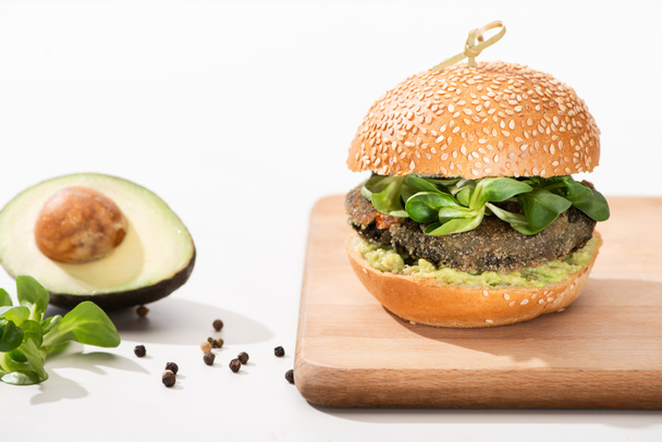 вкусный зеленый веганский бургер с микрозеленью, авокадо, черный перец на деревянной доске на белом фоне
 - Фото, изображение