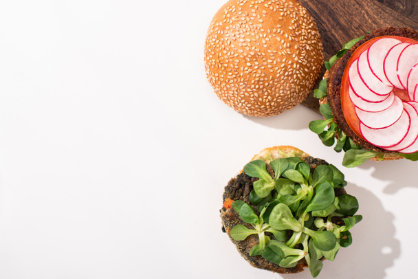 top view of vegan burgers with microgreens, radish on cutting board on white background - Foto, afbeelding