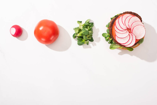 top view of vegan burger with radish, tomato and sprouts on white background - Фото, изображение