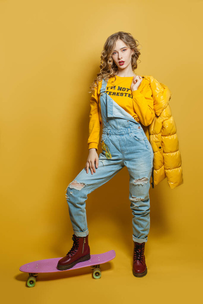 Young woman standing with skateboard on bright yellow background - Photo, Image