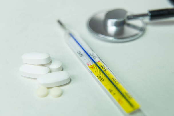 Thermometer, stethoscoop en geneeskunde op witte tafel - Foto, afbeelding