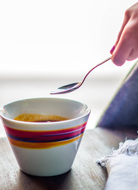 νόστιμη και στον ατμό ζεστή σούπα στο κύπελλο με πολύχρωμες διακοσμήσεις και κορίτσι χέρι κρατώντας κουτάλι - Φωτογραφία, εικόνα