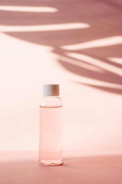 Пластиковая бутылка с розовой розовой водой на пастельном фоне с тропической тенью пальмового листа. Прозрачный тонер и тонер для увлажнения и очищения кожи. Мицеллярная вода или очищающая пена
. - Фото, изображение