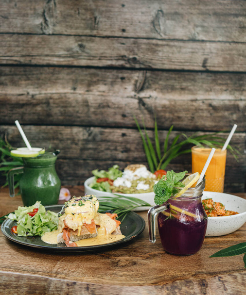Dinner in cafe with eggs benedict, toast with avocado, pasta with shrimps and drinks on wooden background - Fotografie, Obrázek