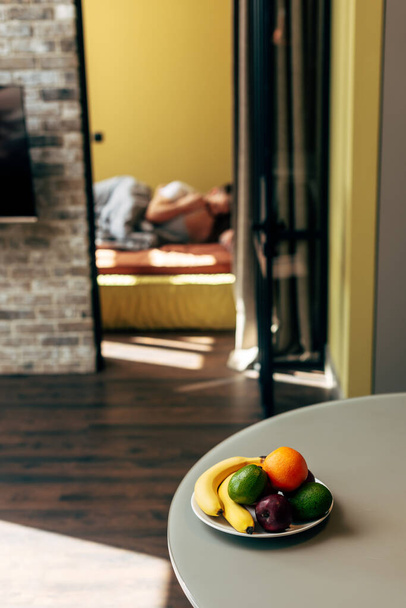 επιλεκτική εστίαση των νόστιμων φρούτων στο τραπέζι κοντά στο ζευγάρι στην κρεβατοκάμαρα  - Φωτογραφία, εικόνα