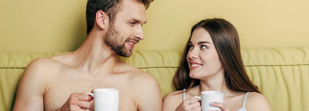 imagen horizontal de pareja feliz mirándose y sosteniendo tazas con café
 - Foto, imagen
