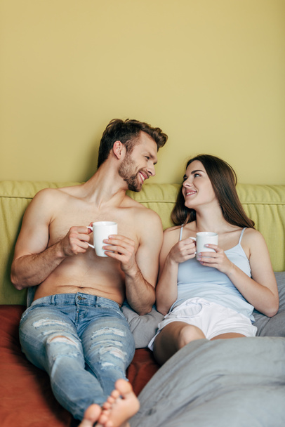 selective focus of happy couple looking at each other and holding cups with coffee - Fotografie, Obrázek