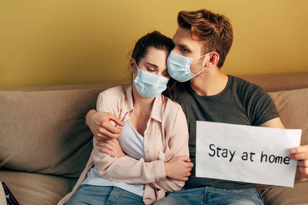 foyer sélectif de l'homme étreignant petite amie dans le masque médical et tenant la plaque avec rester lettrage à la maison
  - Photo, image