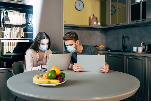 szabadúszók orvosi maszkokban, akik otthonról dolgoznak laptopok közelében  - Fotó, kép
