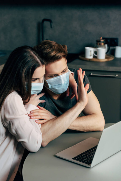selective focus of man in medical mask waving hand while having video chat near girlfriend  - Фото, зображення