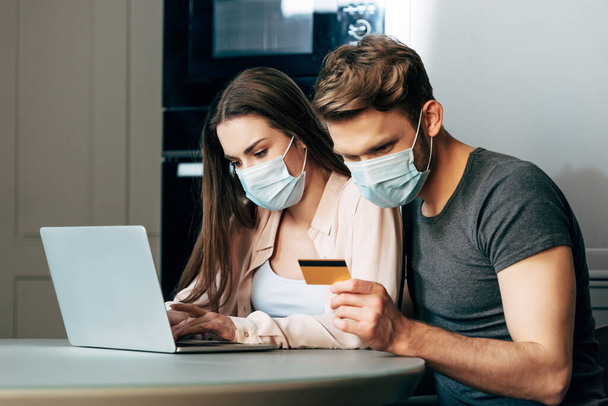 man in medical mask holding credit card while sitting near laptop and girl  - Fotó, kép