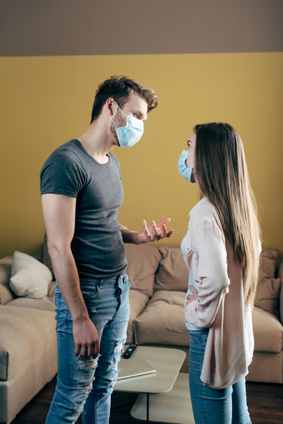 hombre en máscara médica gesto mientras se pelea con la novia en casa
  - Foto, Imagen