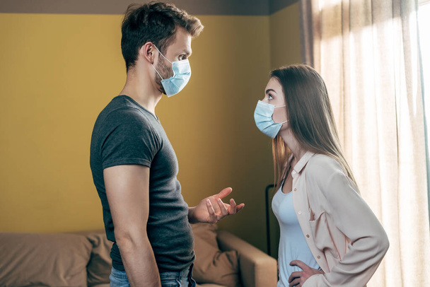 side view of man in medical mask gesturing while quarreling with woman at home  - Фото, зображення