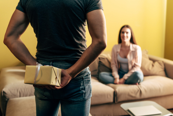 вибірковий фокус людини тримає подарунок позаду подруги у вітальні
  - Фото, зображення
