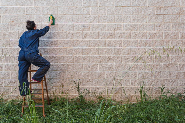 Een vrouw bovenop een ouderwetse trap die de muur gladstrijkt met troffel. ruimte op het recht om te etiketteren.. - Foto, afbeelding