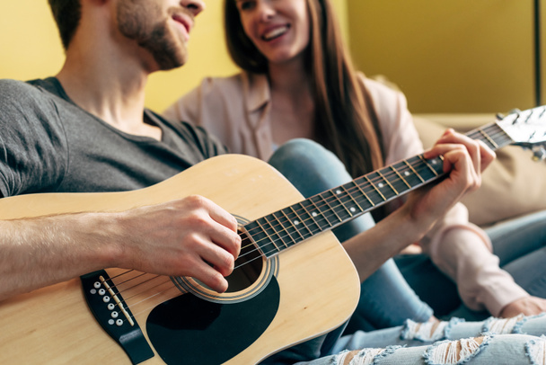 recortado vista de barbudo hombre jugando guitarra acústica cerca feliz chica en sala de estar
  - Foto, imagen