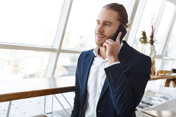 Image of a handsome young businessman indoors in office talking by mobile phone. - Foto, Bild