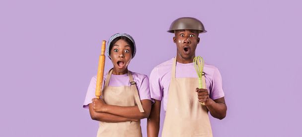 Surpris couple afro-américain avec rouleau à pâtisserie et fouet ayant du mal à cuisiner sur fond de couleur, panorama
 - Photo, image