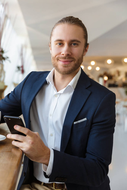 Photo of a positive handsome young businessman indoors in office using mobile phone. - Foto, afbeelding