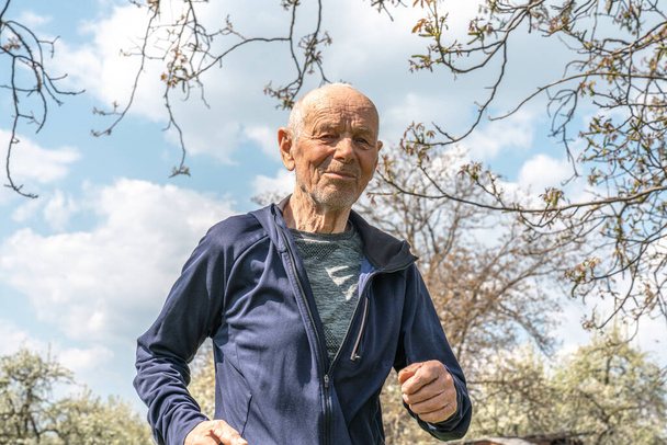 春の晴れた日にはスポーツウェアを着た90歳の男性が庭を走っています - 写真・画像