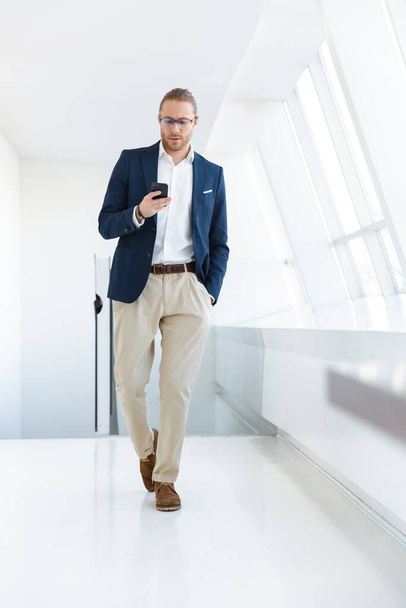 Image of handsome serious young businessman indoors in office using mobile phone. - Fotoğraf, Görsel
