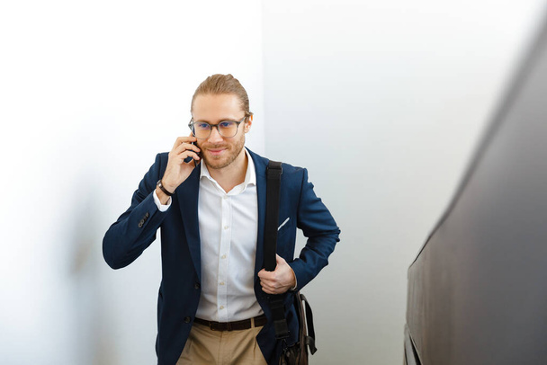 Image of smiling young businessman indoors walking by upstairs talking by mobile phone. - Zdjęcie, obraz