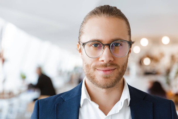 Image of handsome positive pleased young businessman indoors in office looking aside. - Valokuva, kuva