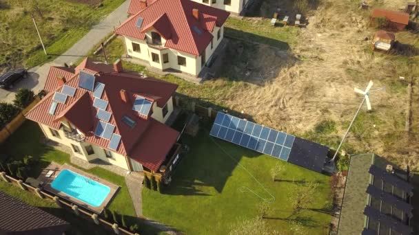 Vista aérea de uma casa privada com jardim coberto de grama verde, painéis solares no telhado, piscina com água azul e gerador de turbinas eólicas. - Filmagem, Vídeo