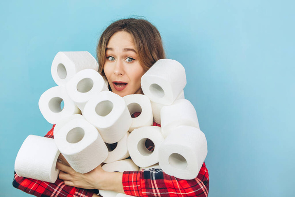 Girl with a lot of rolls of toilet paper in her hands on a blue background. Lack of toilet paper during the coronavirus pandemic. Lack of hygiene products. - Фото, зображення