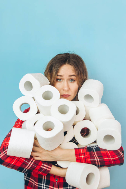 Girl with a lot of rolls of toilet paper in her hands on a blue background. Lack of toilet paper during the coronavirus pandemic. Lack of hygiene products. - Фото, зображення